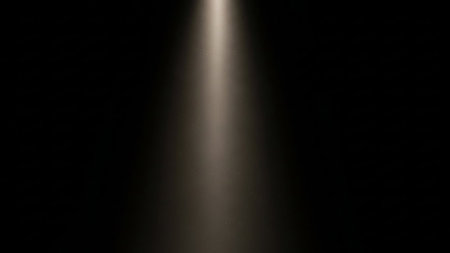 A single, soft beam of light shines downwards from above against a dark background.の素材