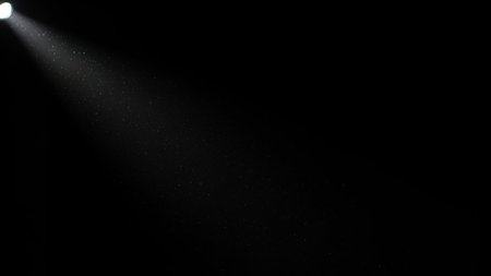 A single spotlight beam shines from the upper left, illuminating dust particles against a dark background.の素材