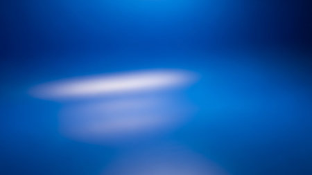 Soft blue abstract background with a blurred, glowing white light orb in the center, creating a dreamy effect.の素材
