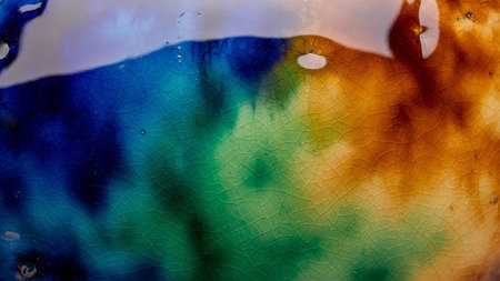 Macro close-up of cracked glaze on ceramic, showcasing vibrant transitions of blue, green, and orange colors with intricate crackle patterns.の素材