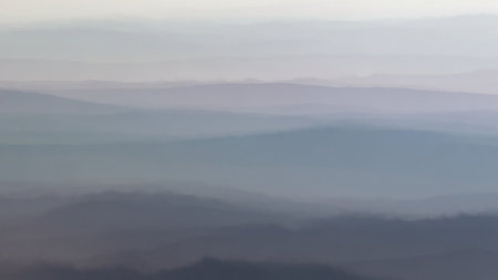 Layers of misty mountains fade into a soft, hazy horizon under a pale sky. Clear details and vibrant colors en...の素材