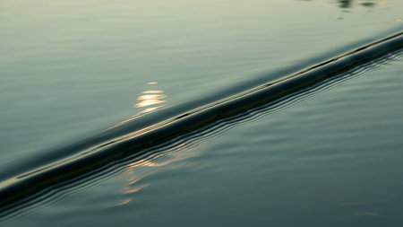 Close-up of gentle ripples on a water surface with a soft sun reflection creating a tranquil abstract pattern.の素材