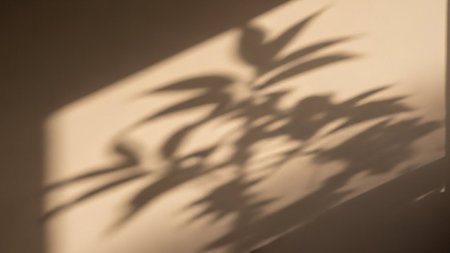 Soft, dappled shadows of palm leaves are cast across a light beige wall, creating a natural, organic pattern.の素材