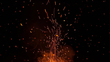 Fiery orange sparks and glowing embers rise and scatter against a dark black background.の素材
