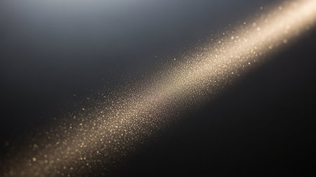 A diagonal beam of bright golden glitter particles sparkles against a dark grey background, creating a magical and festive bokeh effect.の素材