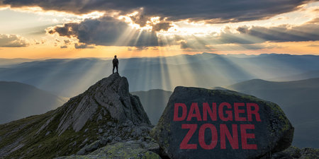 Rock showing hiker on mountain peak overlooking valley with sun rays and danger zone sign on rock keywords: hiker, mountain peak, valley, sun rays,...の素材