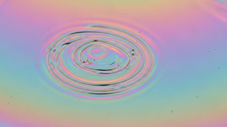 An iridescent oil slick on a water surface creating colorful concentric ripples and patternsの素材