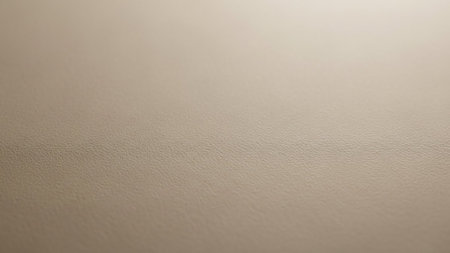 A close-up macro reveals a subtle beige textured surface with a fine grain and a shallow depth of field, creating a soft, neutral background.の素材