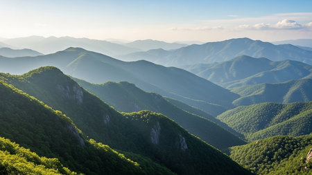Sunlight showing rolling green mountain ranges under a hazy blue sky with soft sunlight illuminating the slopes and valleys creating a serene and...の素材