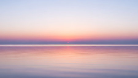 With showing serene ocean horizon at sunrise with soft pastel pink and blue sky reflecting on calm water surface. resolutionの素材