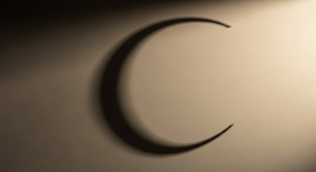 A crescent moon shadow is cast on a textured sepia-toned wall with soft lighting and subtle focus.の素材