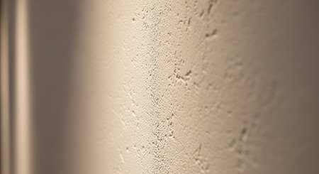 A close-up of a rough, textured off-white wall surface is illuminated by dramatic light, casting strong diagonal shadows that create depth and...の素材