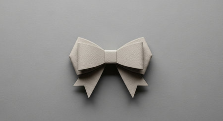 A minimalist folded paper bow with a subtle texture sits on a plain gray background.の素材