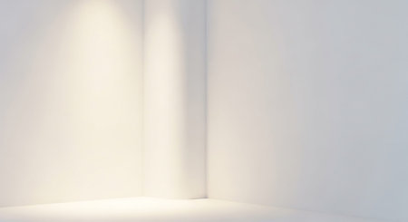 The corner of a bright white room is softly illuminated by warm light, casting subtle shadows on the walls and floor, creating a clean and...の素材