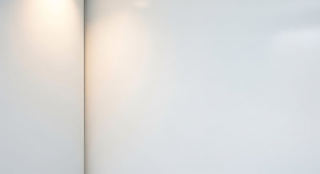 A minimalist interior corner featuring a bright white wall with soft warm light casting subtle shadows and highlights.の素材