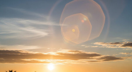 A bright sun with a prominent lens flare illuminates a blue sky filled with wispy clouds, suggesting a sunset or sunrise.の素材