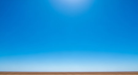A vast, clear, bright blue sky stretches above a flat, brown earth horizon under the intense light of the sun.の素材