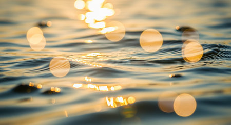 Close-up view of a water surface with gentle ripples, reflecting golden sunlight in soft bokeh circles, creating a serene and shimmering effect.の素材