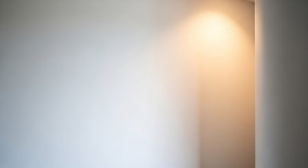 A plain white wall is illuminated by a soft, warm light creating a subtle gradient and shadow.の素材