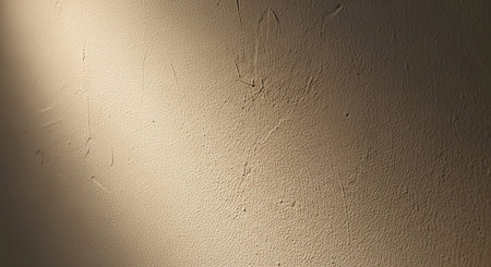 A close-up view of a textured beige wall with a soft diagonal light casting subtle shadows.の素材