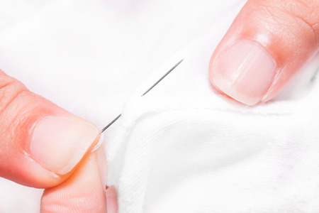 women's hands while sewing white clothの写真素材