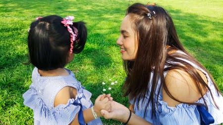 child give flower to mom on green grass in park