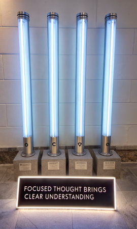 Four futuristic, glowing blue lightsaber props are showcased on individual concrete bases within a museum setting, representing iconic cinematic weaponry, perfect for fan collections and sci-fi enthusiasts.の素材
