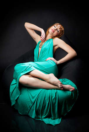 Woman in evening dress reclining on a chair on black backgroundの写真素材