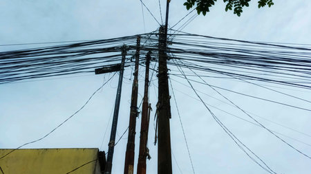 Messy and Tangled Network of Electrical and Telecommunication Cables on Concrete Utility Poles Against a Clear Skyの写真素材