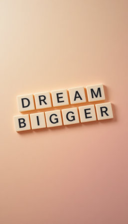 This image features scrabble tiles spelling "DREAM BIGGER" on a soft pastel background, ideal for conveying motivation and inspiration in your projects.の素材