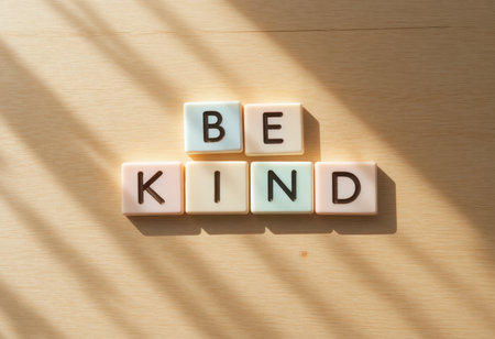 A serene arrangement of letter blocks spelling 'BE KIND,' showcasing a gentle message of positivity. Soft sunlight casts elegant shadows, creating a warm atmosphere.の素材