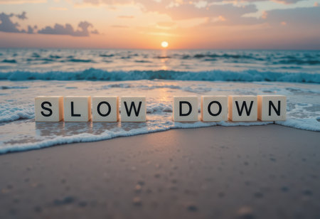 A serene beach scene at sunset featuring the motivational message "slow down" arranged in block letters, captured amidst gentle ocean waves and soft sand.の素材