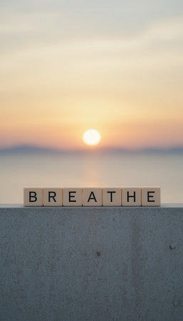 The image features wooden blocks arranged to spell "BREATHE" against a serene sunset over calm water. This symbolizes peace, mindfulness, and tranquility.の素材