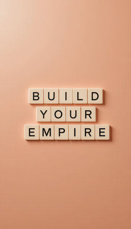 Inspirational message "Build Your Empire" displayed with letter tiles on a soft peach background, ideal for themes of motivation and success in business and personal growth.の素材
