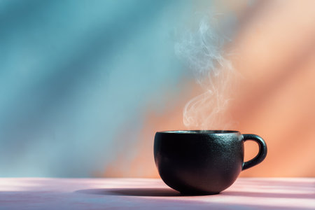 A close-up of a steaming black ceramic cup set against a colorful pastel background, evoking a sense of warmth and comfort. Ideal for beverage themes.の素材