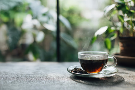 A steaming cup of black tea sits on a gray surface, surrounded by lush greenery. The scene evokes a sense of calm and relaxation, perfect for cozy moments.の素材