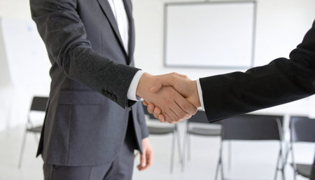 Two business professionals engage in a handshake during a formal meeting, symbolizing partnership and cooperation in a corporate environment.の素材