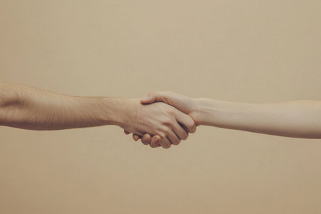 A close-up image depicting two hands shaking in agreement, set against a neutral background, symbolizing trust, partnership, and professional collaboration.の素材