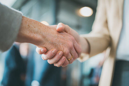 A close-up view of two individuals shaking hands in a contemporary office. This handshake symbolizes agreement, collaboration, and trust in a professional environment.の素材