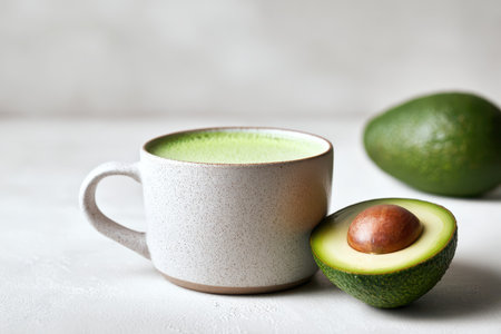 A stylish cup filled with a smooth green beverage sits beside a fresh avocado half, showcasing vibrant colors and a healthy lifestyle aesthetic.の素材
