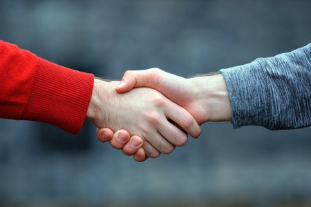 Two hands engage in a handshake, symbolizing trust and collaboration. The background is softly blurred to emphasize the connection between individuals.の素材