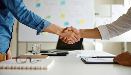 Two professionals engage in a handshake, symbolizing a successful business partnership and collaboration in a modern office setting.の素材