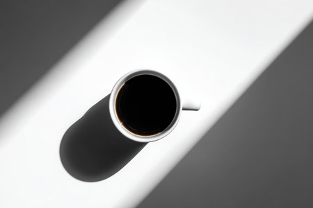 A minimalist coffee cup filled with black coffee casts a shadow on a bright white surface, creating a striking contrast that emphasizes simplicity and elegance.の素材