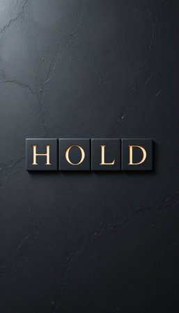 This image features a sleek black surface with four tiles displaying the word "HOLD" in elegant gold letters. The minimalist design emphasizes contrast and sophistication.の素材