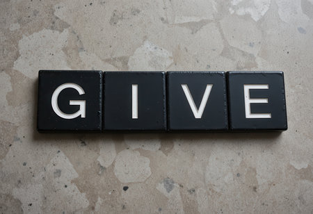 Close-up of the word "GIVE" displayed on black tiles against a textured surface, conveying a minimalist artistic message with a modern touch.の素材