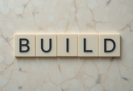 Close-up view of word tiles spelling "BUILD" arranged on a smooth marble surface. This image represents concepts of construction, growth, and development in various contexts.の素材