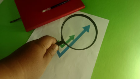 Hand with a magnifying glass and a pencil on a green backgroundの写真素材