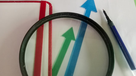 Magnifying glass and red and blue arrows on a white sheet of paperの写真素材