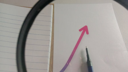 Magnifying glass and pen on a white sheet of paper with an arrow