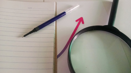 Magnifying glass and pen on the notebook with red arrow going upの写真素材